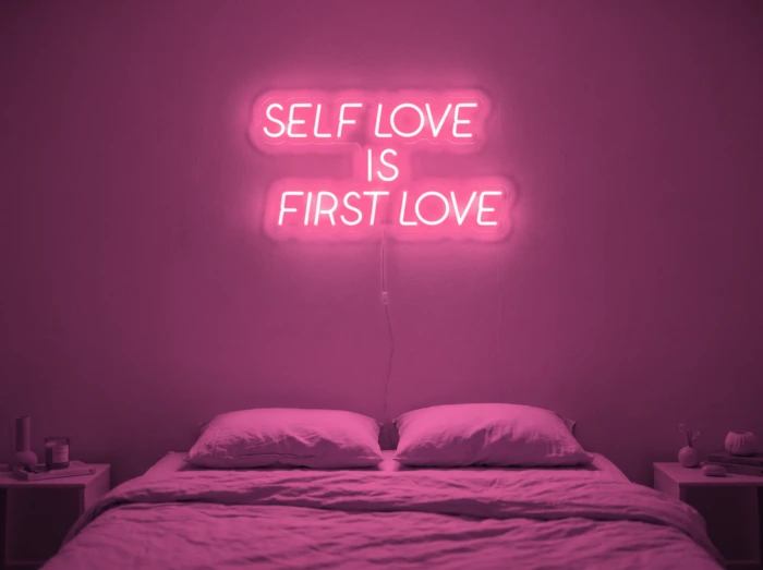 Neonskylt «Self Love Is First Love» i rosa LED-neon, monterad på vägg
