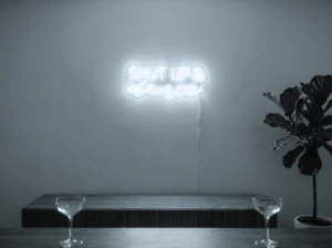 Neonskylt «Shut Up And Dance» i iskall vit LED-neon, monterad på vägg