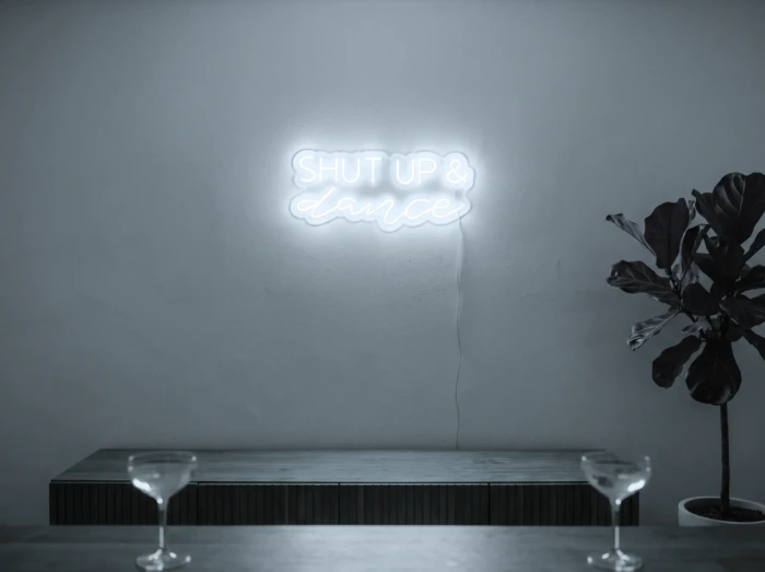 Neonskylt «Shut Up And Dance» i iskall vit LED-neon, monterad på vägg