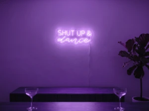 Neonskylt «Shut Up And Dance» i lila LED-neon, monterad på vägg