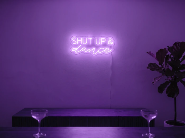 Neonskylt «Shut Up And Dance» i lila LED-neon, monterad på vägg