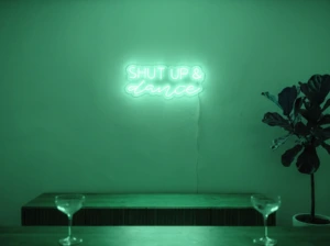 Neonskylt «Shut Up And Dance» i mintgrön LED-neon, monterad på vägg