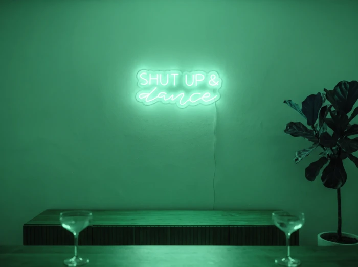 Neonskylt «Shut Up And Dance» i mintgrön LED-neon, monterad på vägg