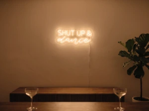 Neonskylt «Shut Up And Dance» i orange LED-neon, monterad på vägg