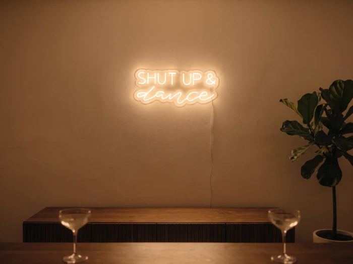 Neonskylt «Shut Up And Dance» i orange LED-neon, monterad på vägg