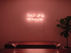 Neonskylt «Shut Up And Dance» i röd LED-neon, monterad på vägg