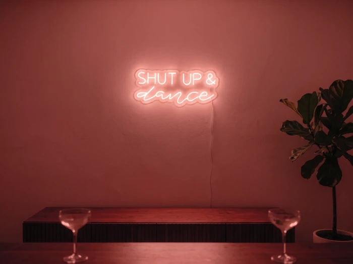 Neonskylt «Shut Up And Dance» i röd LED-neon, monterad på vägg