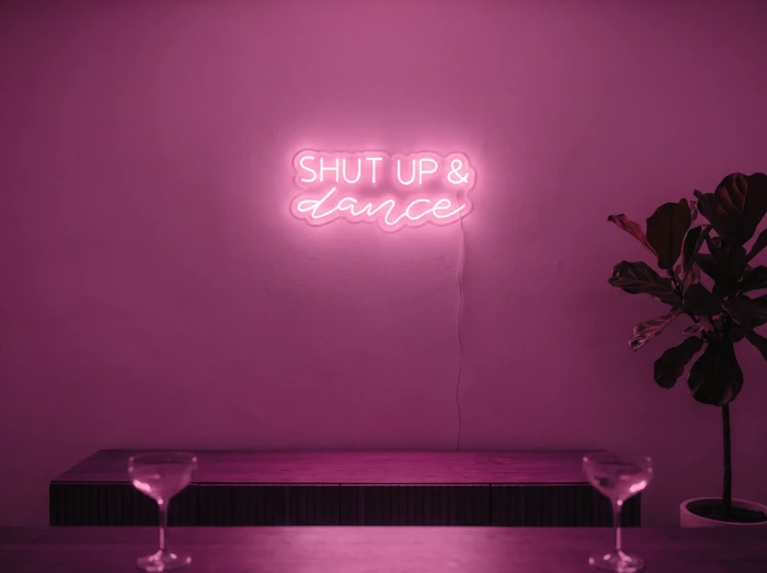 Neonskylt «Shut Up And Dance» i rosa LED-neon, monterad på vägg
