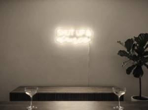 Neonskylt «Shut Up And Dance» i varmvit LED-neon, monterad på vägg