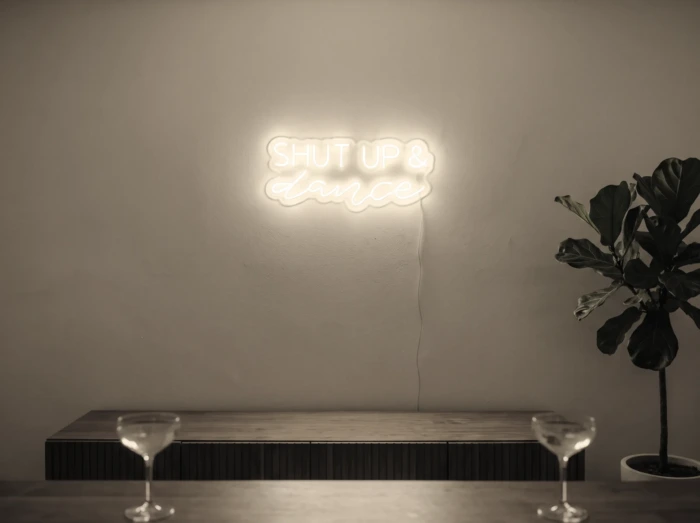 Neonskylt «Shut Up And Dance» i varmvit LED-neon, monterad på vägg