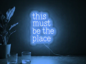 Neonskylt «This Must Be The Place» i isblå LED-neon, monterad på vägg