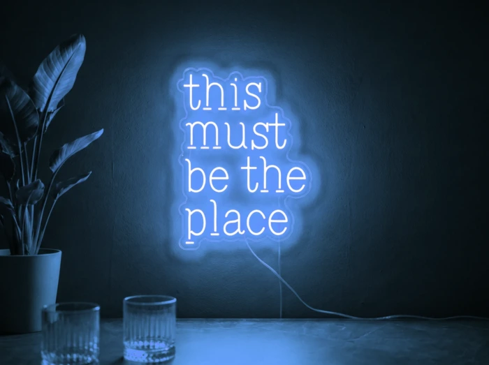 Neonskylt «This Must Be The Place» i isblå LED-neon, monterad på vägg