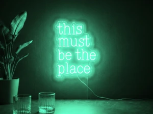 Neonskylt «This Must Be The Place» i mintgrön LED-neon, monterad på vägg