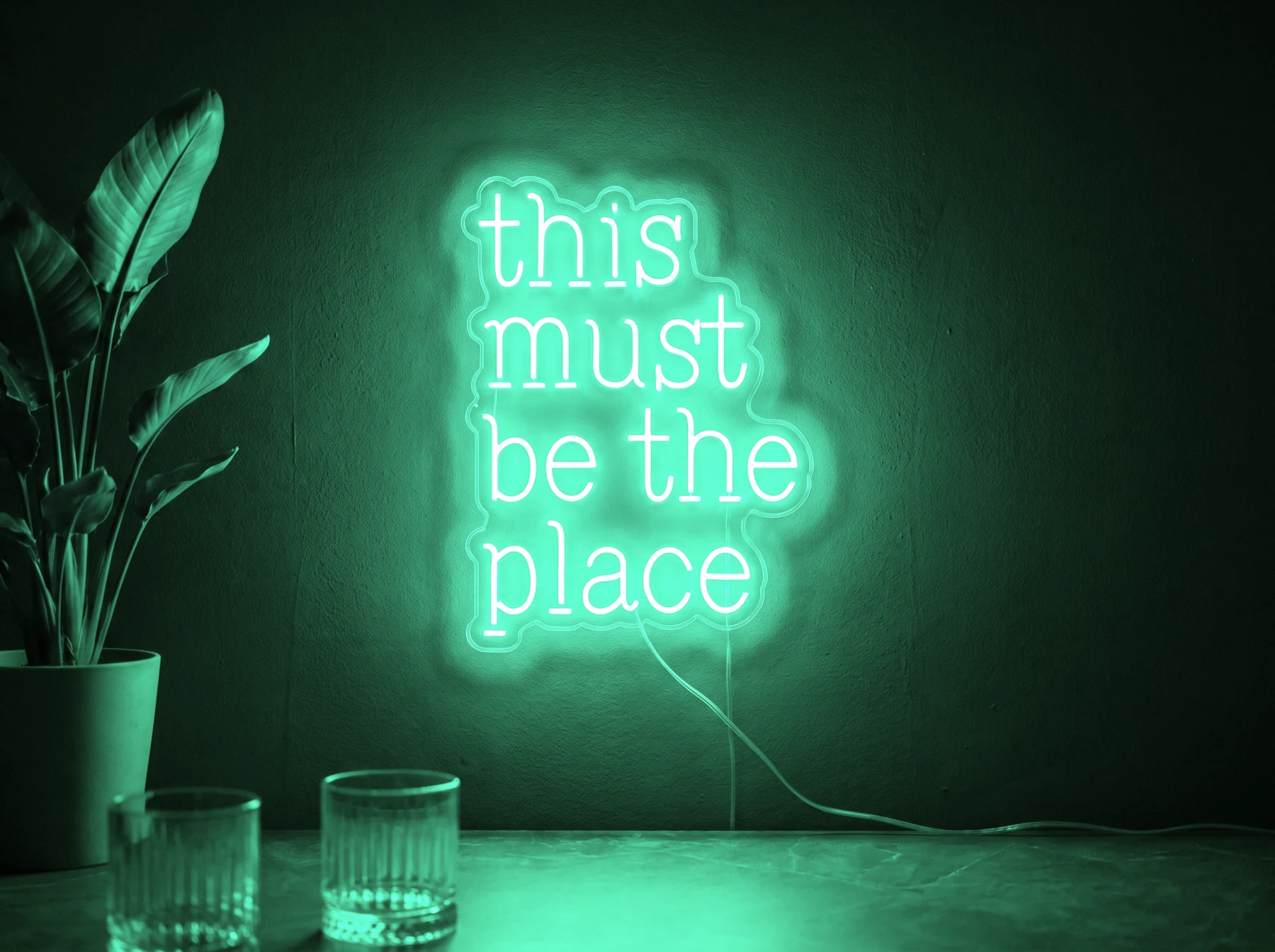Neonskylt «This Must Be The Place» i mintgrön LED-neon, monterad på vägg