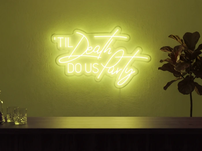 Neonskylt «Til Death Do Us Party» i gul LED-neon, monterad på vägg
