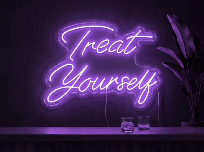 Neonskylt «Treat Yourself» i lila LED-neon, monterad på vägg