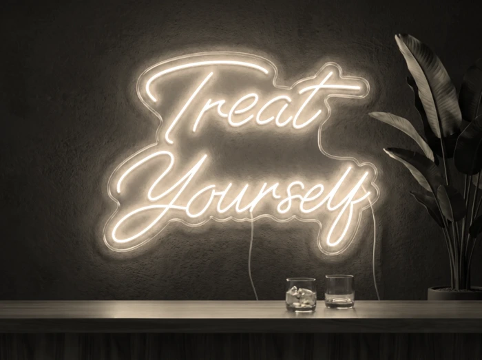 Neonskylt «Treat Yourself» i varmvit LED-neon, monterad på vägg