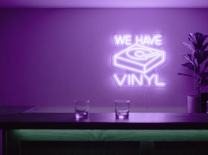 Neonskylt «We Have Vinyl» i lila LED-neon, monterad på vägg