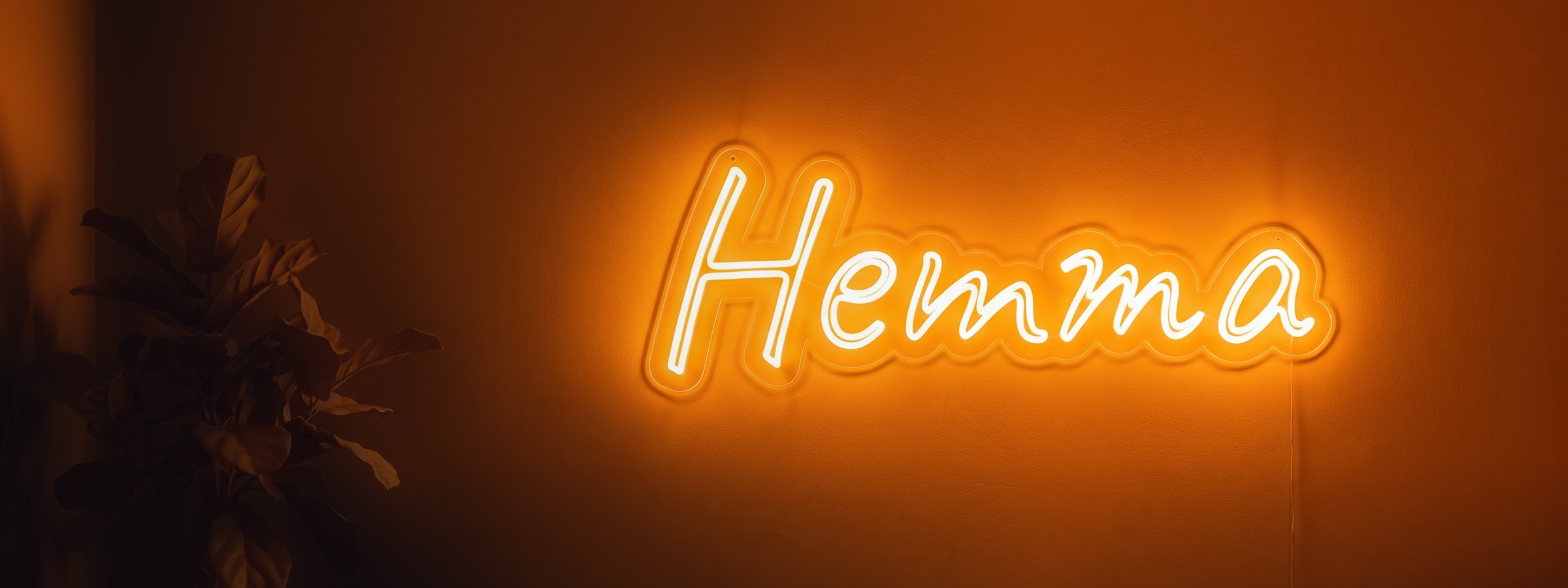 Neonskylt med texten Hemma i varmvitt LED-neon på väggen i ett vardagsrum